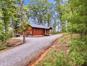 A wooden cabin with a gravel driveway, surrounded by trees.