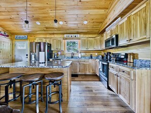 A kitchen with wooden cabinets, stainless steel appliances, a granite countertop, and a bar area with stools.