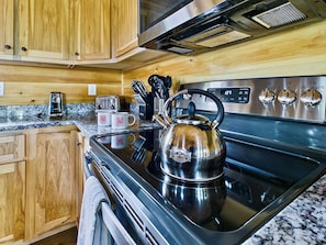 A kitchen with wooden cabinets, a stainless steel stove, a kettle, and a toaster.
