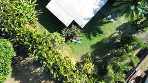 An aerial view of a house surrounded by lush greenery, including palm trees and various shrubs.