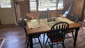 Une salle à manger en bois avec une table dressée pour quatre personnes, entourée de chaises.