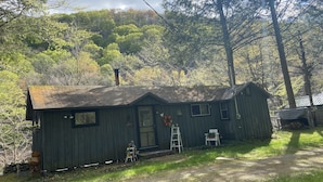 Une cabane rustique avec un toit en pente, une porte d’entrée et un petit porche équipé d’une chaise et d’une échelle.