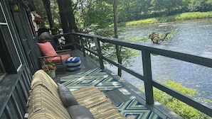 Une terrasse en bois avec un canapé et des coussins, donnant sur une rivière.