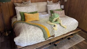 Une pièce aux murs lambrissés, avec un lit agrémenté d’une literie à motifs, d’un plaid vert tricoté et d’un coussin vert en forme de grenouille.