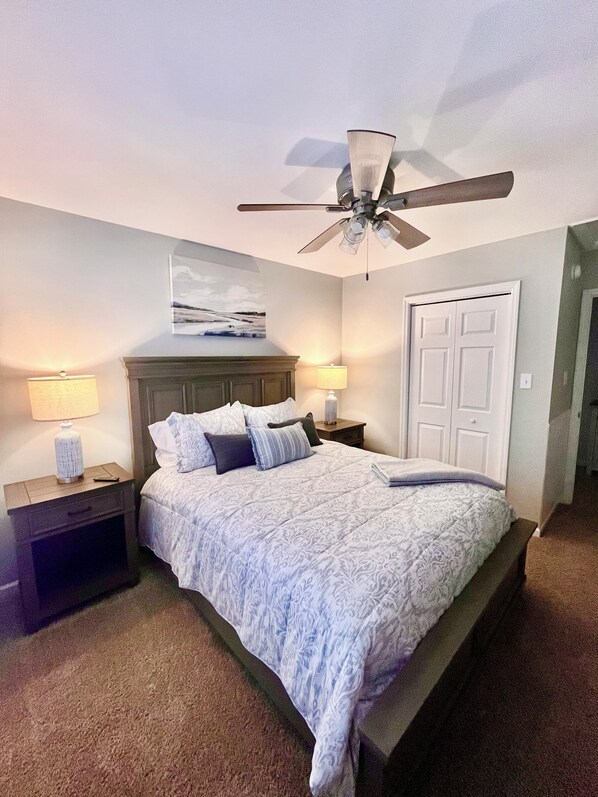 A bedroom with a bed, two bedside tables, a ceiling fan, a door, and a painting on the wall.