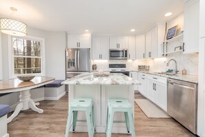Una cocina moderna con armarios blancos, una isla de mármol, electrodomésticos de acero inoxidable y una ventana con vistas a árboles.