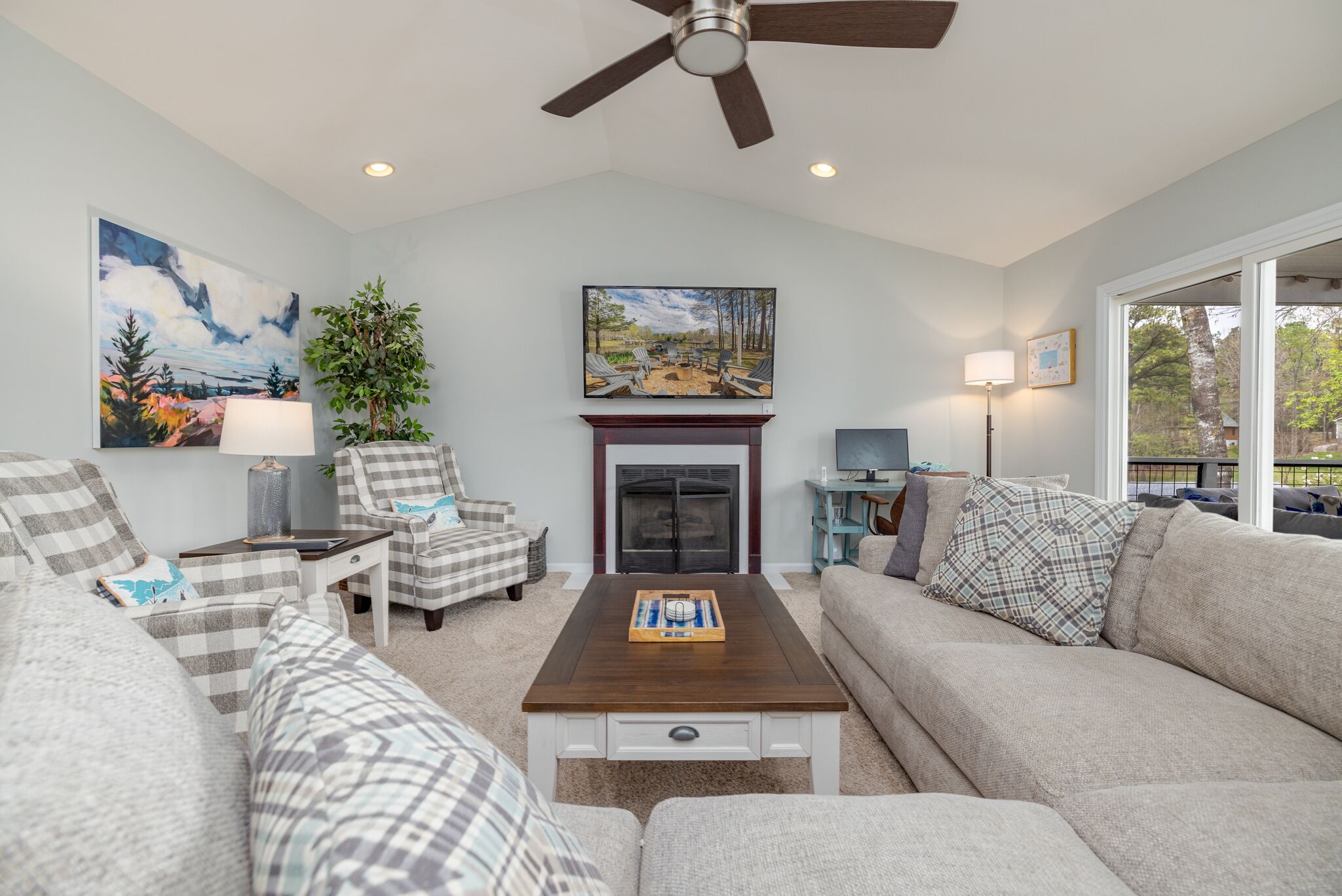 A living room with a fireplace, a ceiling fan, and a large window.