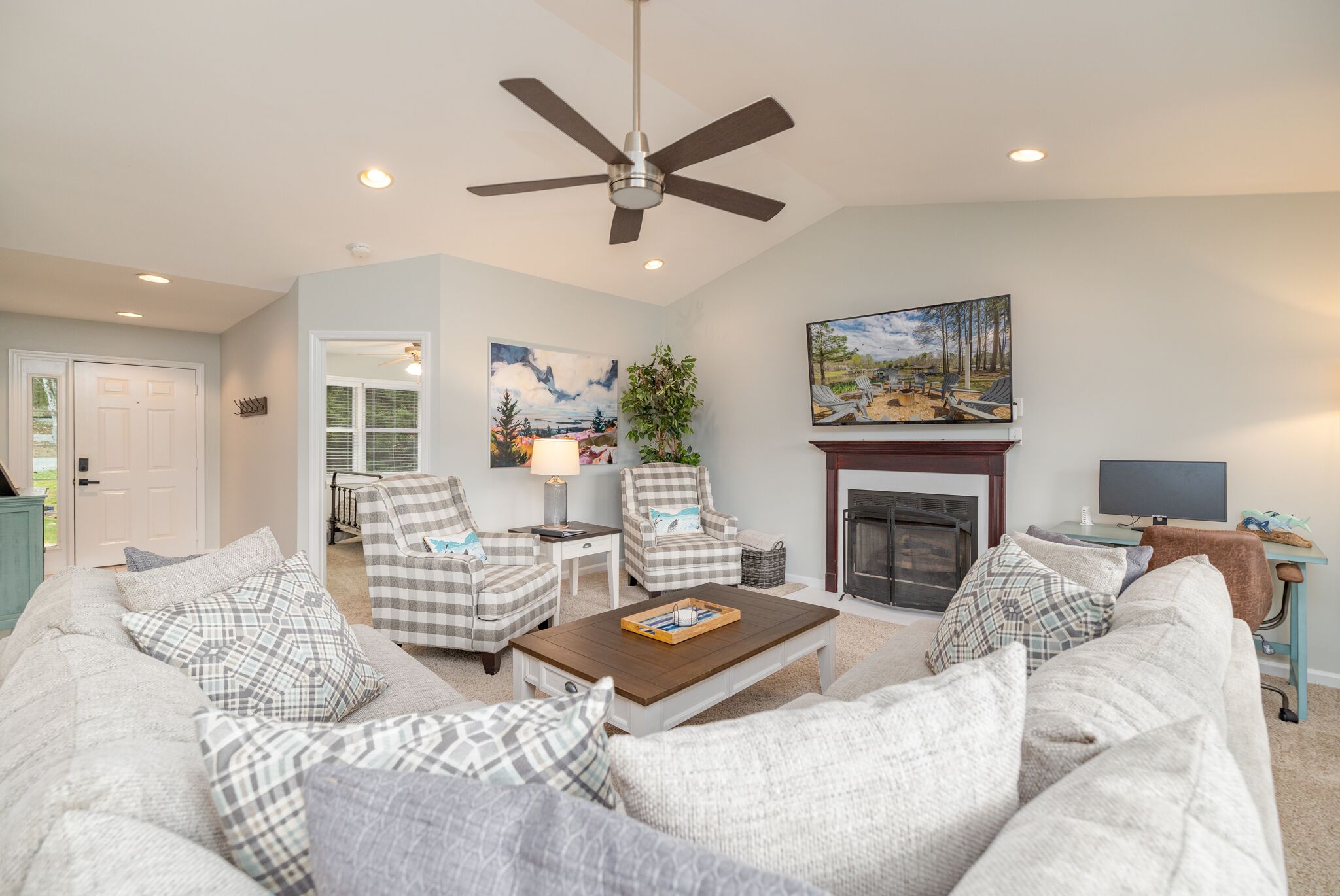 A living room with a sofa set, two armchairs, a coffee table, a fireplace, a painting, and a ceiling fan.
