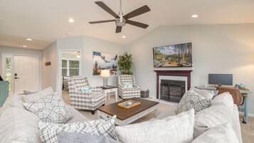 A living room with a sofa set, two armchairs, a coffee table, a fireplace, a painting, and a ceiling fan.