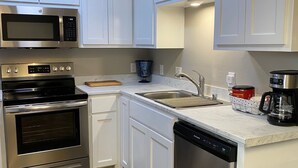 A modern kitchen with white cabinets, stainless steel appliances, a microwave, oven, dishwasher, and a coffee maker.