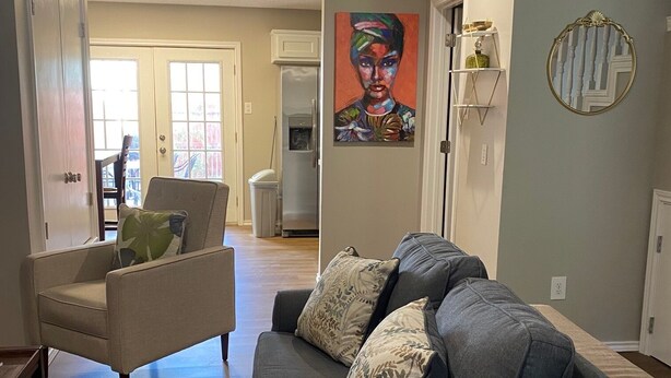 A living room with a grey sofa, a beige armchair, and a dining area in the background.