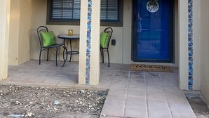 A building with a blue door, two windows with blinds, a balcony with decorative railing, and a small table with chairs.