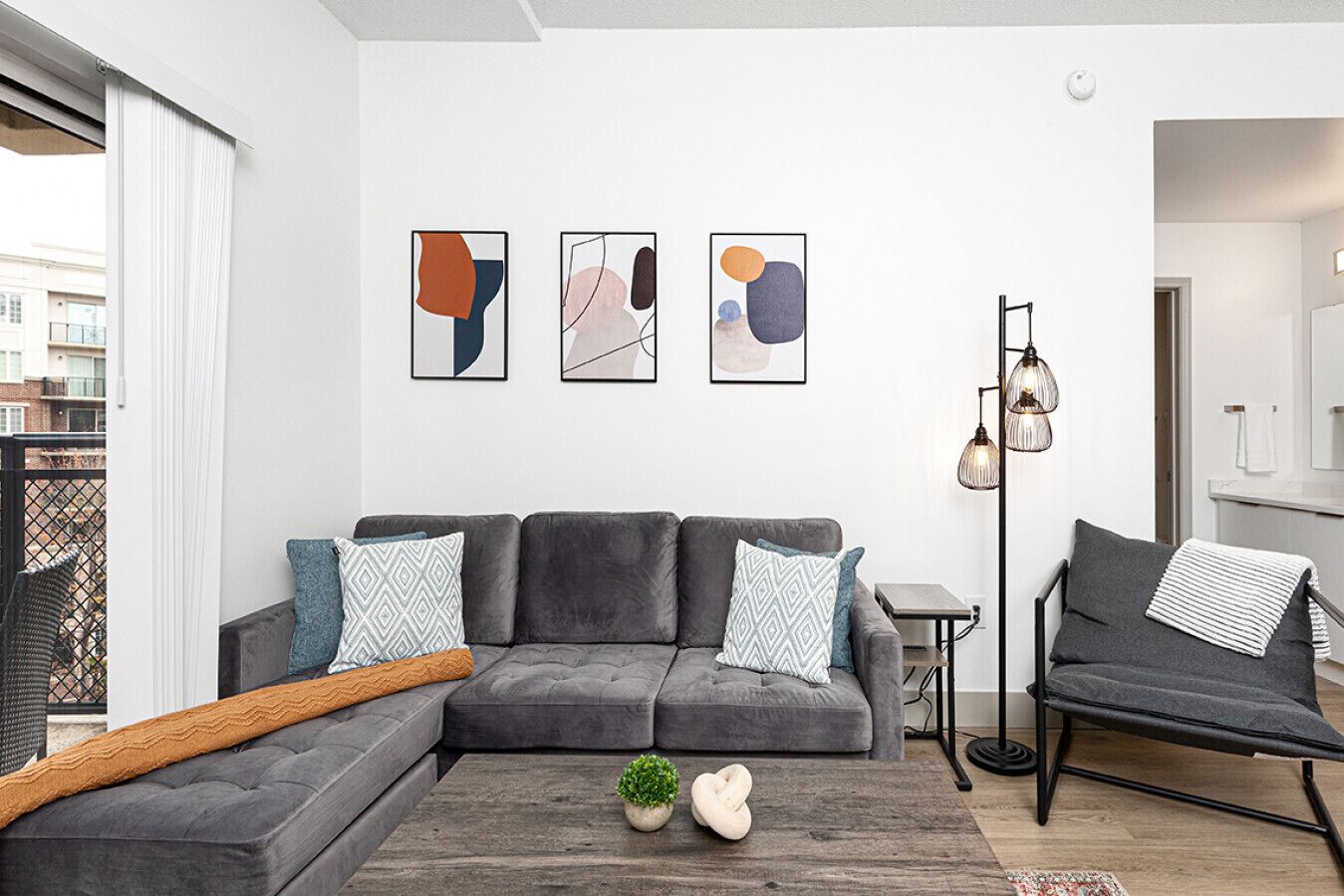 Uma sala de estar moderna com um sofá modular cinza, uma mesinha lateral e um abajur. Há obras de arte abstratas nas paredes acima do sofá.