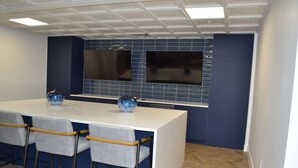 A modern kitchen with a white countertop, blue backsplash, and a built-in microwave. There are four bar stools with grey fabric seats and wooden armrests. - Brand New Luxe Apt | 2Mins to Stadium, Free Parking & WiFi, City Views (Charlotte)