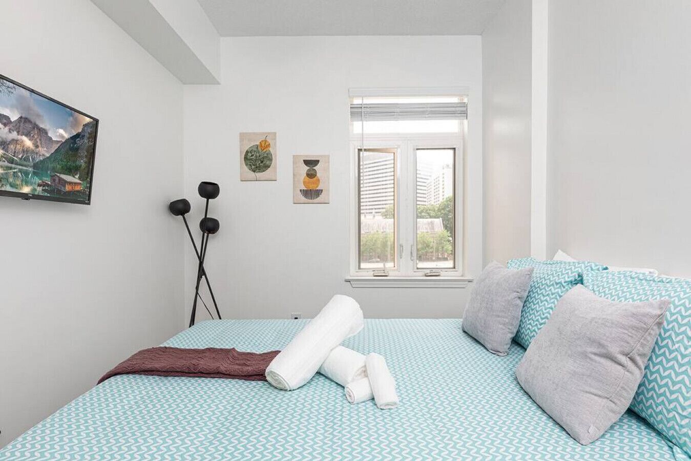 Een slaapkamer met een bed, kussens, een raam en kunst aan de muur.