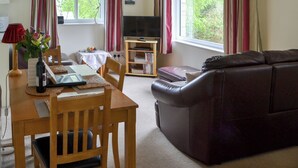 Una sala de estar con una mesa de comedor de madera, un sofá de cuero, un televisor sobre un mueble bajo y una ventana con cortinas.