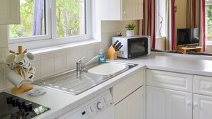 Una cocina moderna con gabinetes blancos, un lavamanos de acero inoxidable, un microondas y un televisor pequeño.