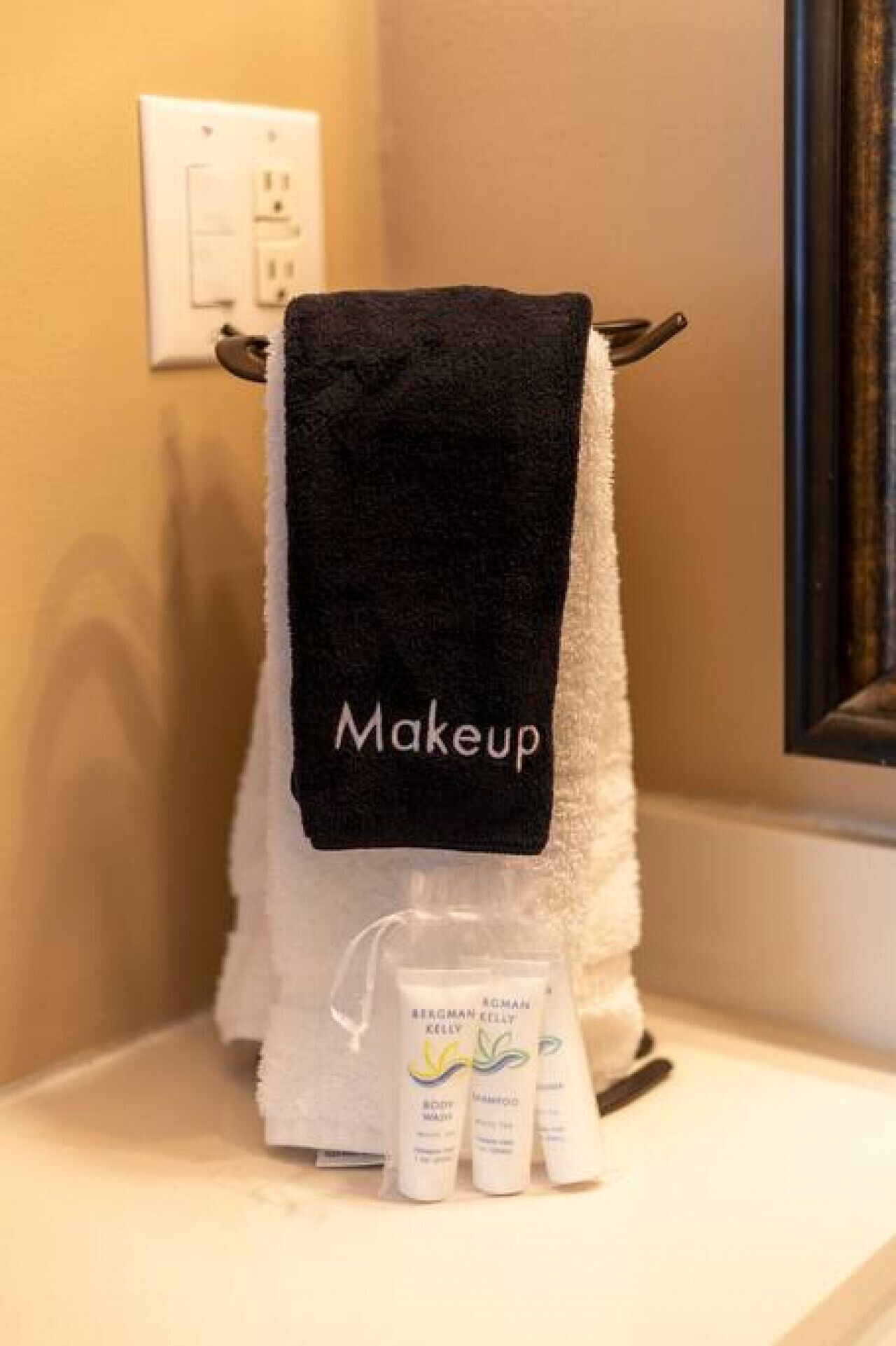 A bathroom with a towel rack holding a black towel labeled 'Makeup' and a set of toiletries on the counter.