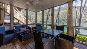 A covered outdoor area with a table and chairs, a sofa, and a staircase leading to an upper level. - Golf & Lake View Retreat - Rumbling Bald Resort Amenities, Sleeps 6 (Lake Lure)