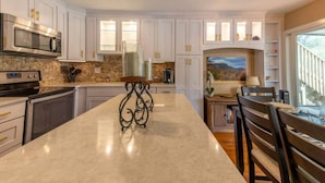 A spacious kitchen with white cabinets, a large island, and a dining area with a view. - Golf & Lake View Retreat - Rumbling Bald Resort Amenities, Sleeps 6 (Lake Lure)