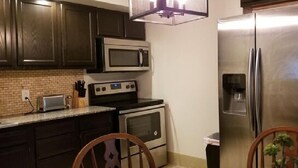 A compact kitchen with dark wooden cabinets, a stainless steel refrigerator, a microwave, an oven, and a toaster. - AV    Bungalows   #2 (Arcadia)