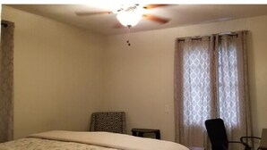 A bedroom with a bed, a ceiling fan, a chair, and a window with curtains. - AV    Bungalows   #2 (Arcadia)