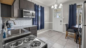 Una cocina moderna con estufa de acero inoxidable, microondas y un lavabo. Hay un comedor con una mesa y sillas.
