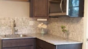 Una cocina con armarios de madera oscura, un lavamanos de acero inoxidable y un microondas.