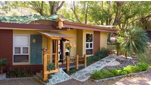 A small, single-story house with a porch, a small garden, and a pathway leading to the entrance. - ARANJUEZ LOFTS - Tree Loft #6 (Santa Ana)