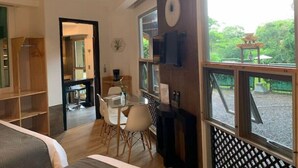 A modern room with a ceiling fan, a dining area with chairs and a table, a large window with a view of greenery, and a clock on the wall. - ARANJUEZ LOFTS - Tree Loft #6 (Santa Ana)