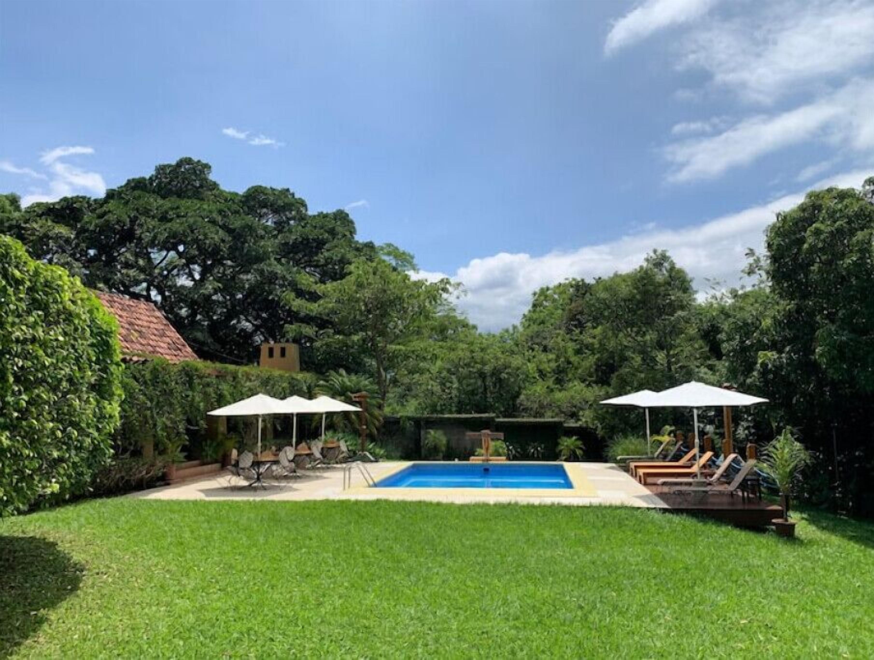 Un patio trasero con piscina, dos sombrillas y sillas de descanso.