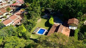 An aerial view of a residential area with a swimming pool surrounded by lush greenery and neighboring houses. - ARANJUEZ LOFTS - Maya Loft #8 (Santa Ana)