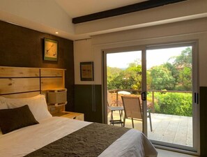 A bedroom with a large bed, wooden headboard, and a sliding glass door leading to a balcony with outdoor furniture.