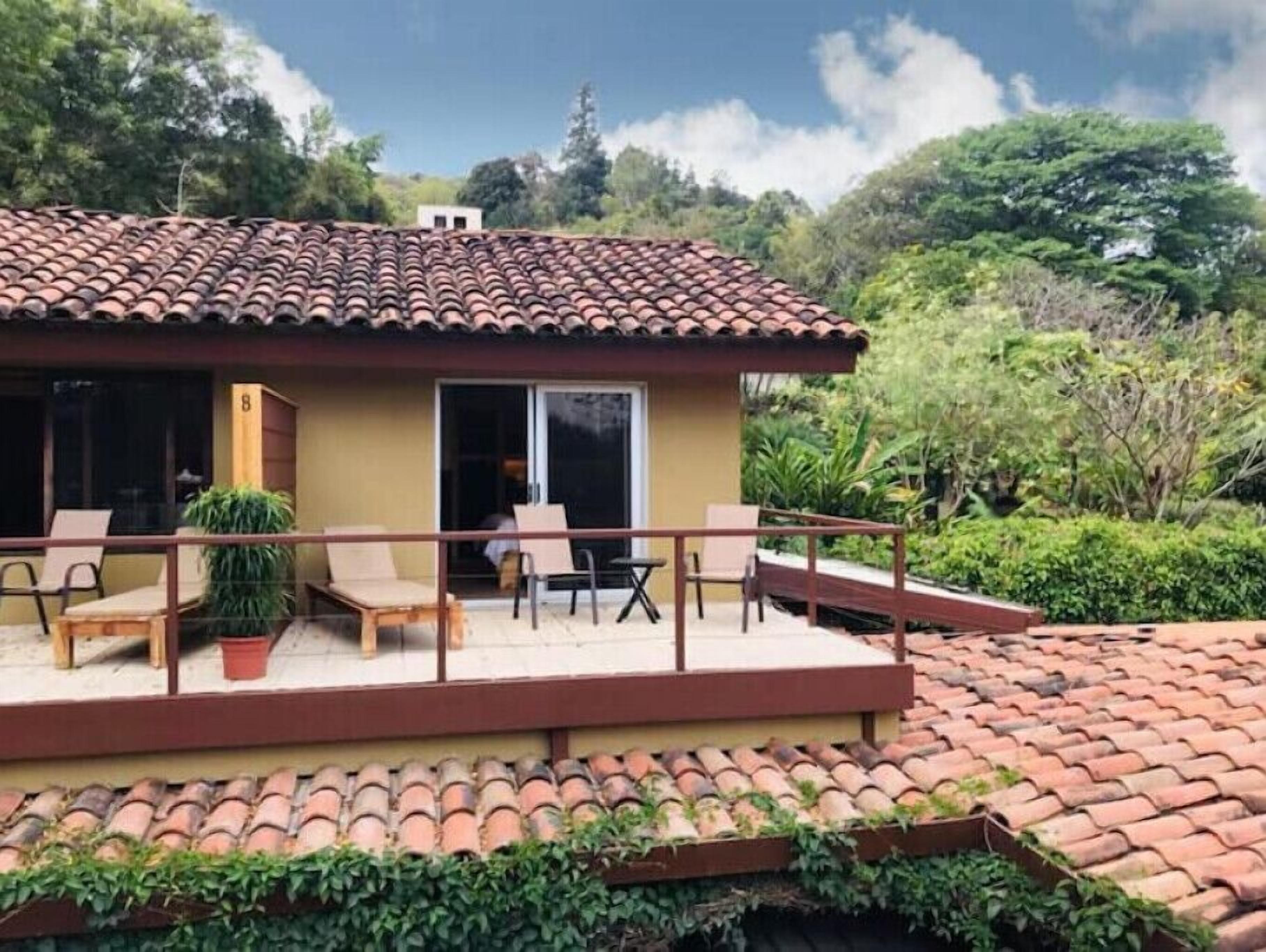 Una casa con techo de tejas, un porche cubierto con sillas y una mesa, y una puerta que da a un espacio resguardado.