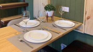 Una mesa de comedor dispuesta con platos, vasos y cubiertos, rodeada de bancos de madera y una planta en maceta.