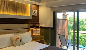 Un dormitorio moderno con una cama grande, cabecera de madera, mesita de noche con lámpara y vista al exterior a través de un ventanal corredero.