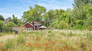 Ein ländliches Haus mit einem Garten voller Wildblumen und einem großen Baum im Hintergrund.