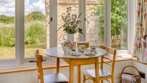 Ein runder Esstisch mit vier Stühlen, eine Vase mit violetten Blumen und ein Teeservice.
