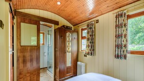 Ein Schlafzimmer mit Holzbalkendecke, einem Bett, einer zur Toilette führenden Tür und einem mit Vorhängen versehenen Fenster.