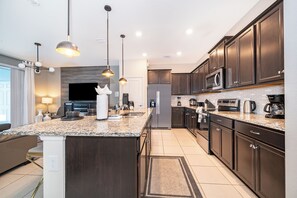 Une cuisine moderne avec des meubles en bois foncé, un plan de travail en granit, des appareils électroménagers en acier inoxydable et des luminaires suspendus.