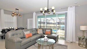 Ein modernes Wohnzimmer mit einem grauen Ecksofa, einem Glastisch und einem Essbereich mit Tisch für vier Personen.
