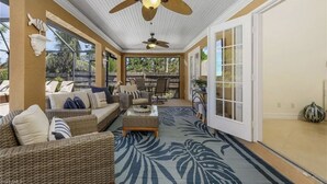 Ein überdachter Patio-Bereich mit Korbmöbeln, Deckenventilatoren und einem großen Fenster.