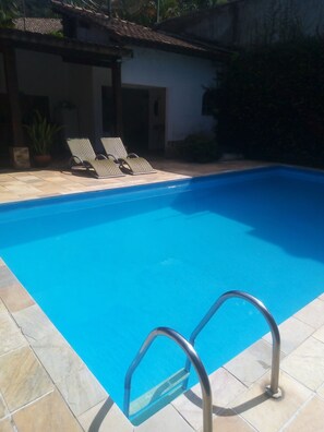 En swimmingpool med metalstige, fliseterrasse og liggestole.