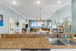 A spacious kitchen with granite countertops, a stainless steel sink, and a dining area with a view.