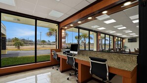 A reception desk with a computer, two chairs, and a view of a parking lot and palm trees. - Quality Inn Yemassee - Point South I-95 (Yemassee)