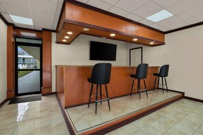 Uma área de recepção com balcão de madeira, três banquetas pretas, uma televisão de tela plana na parede e uma porta que dá para o exterior.