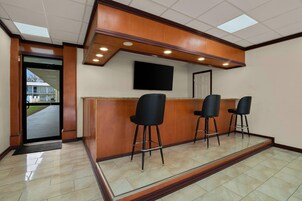 Zona de recepción con mostrador de madera, tres taburetes negros, un televisor de pantalla plana montado en la pared y una puerta que da al exterior.