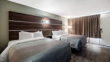 A hotel room with two beds, a wooden headboard, a bedside table, a lamp, and a window with curtains.