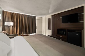 A hotel room with a bed, a desk, a flat-screen TV, a microwave, and a refrigerator.