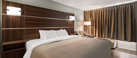 A hotel room with a large bed, wooden headboard, bedside tables, a desk, a chair, a lamp, and a window with curtains.